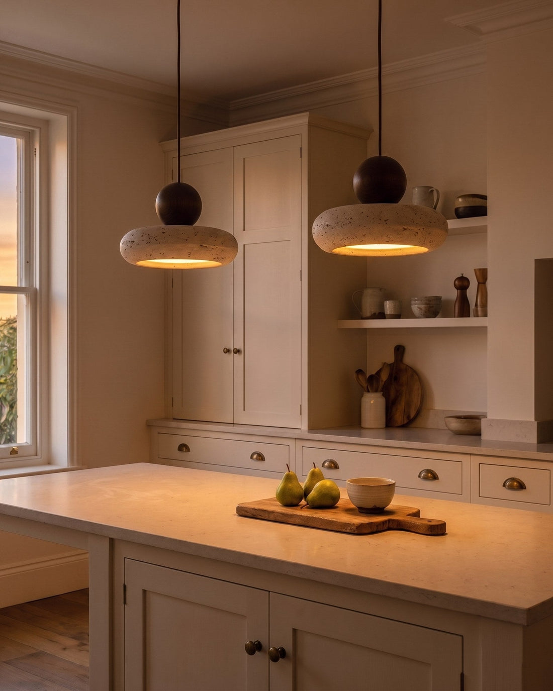 A pair of natural stone pendants glowing over a kitchen island at dusk