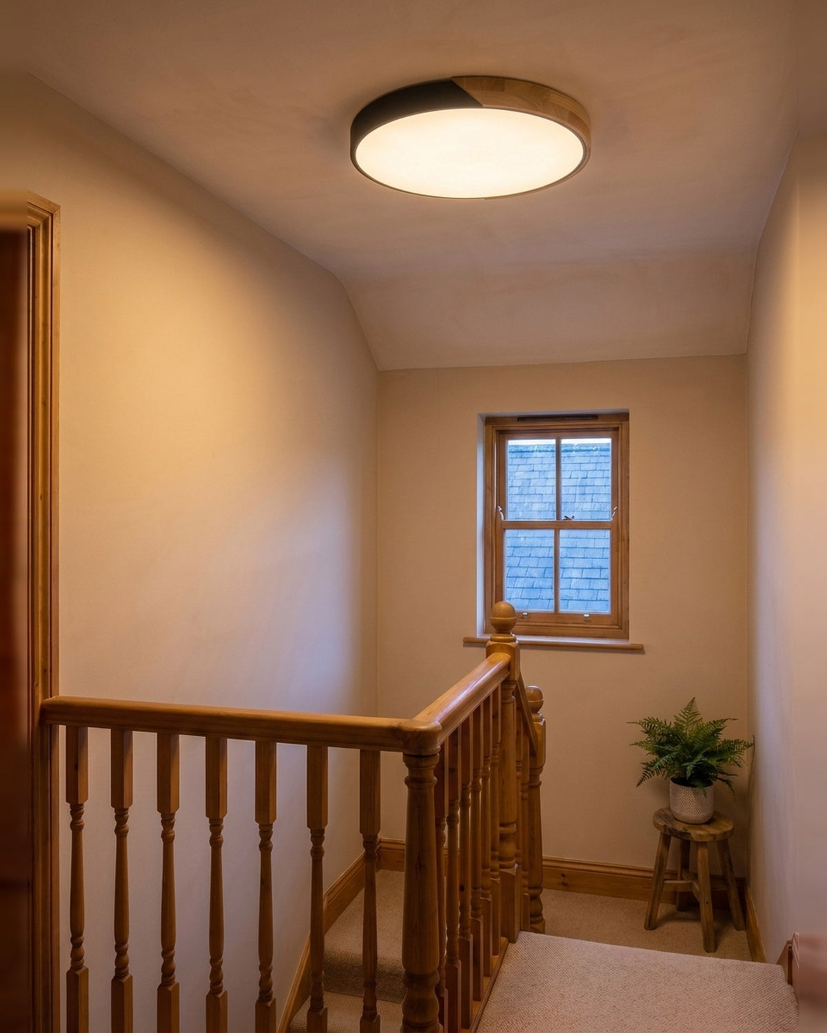 Black ultra-thin wood-trimmed ceiling light glowing warm on a landing at early evening