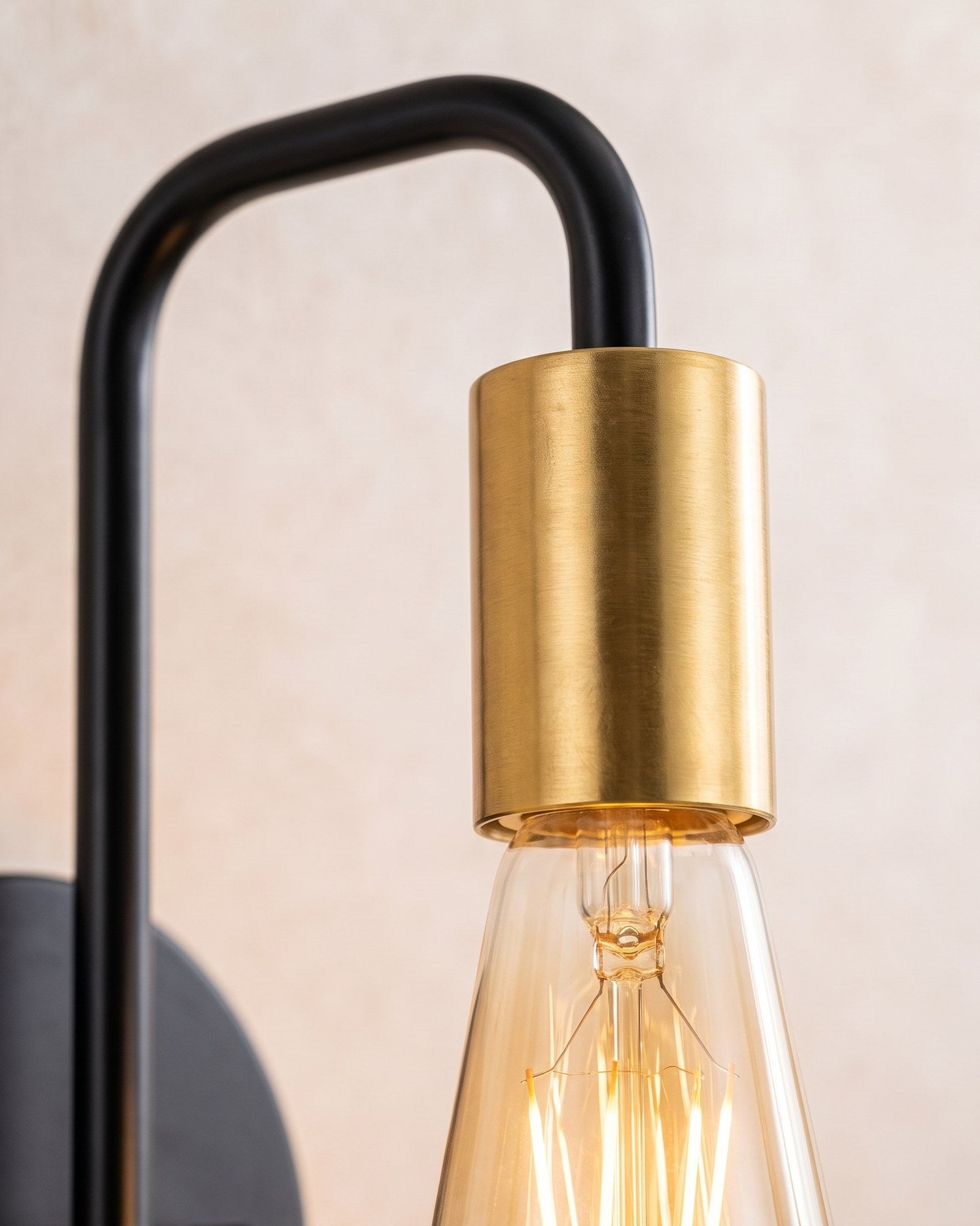 Macro of the brass socket and glowing amber filament bulb on the black hook arm