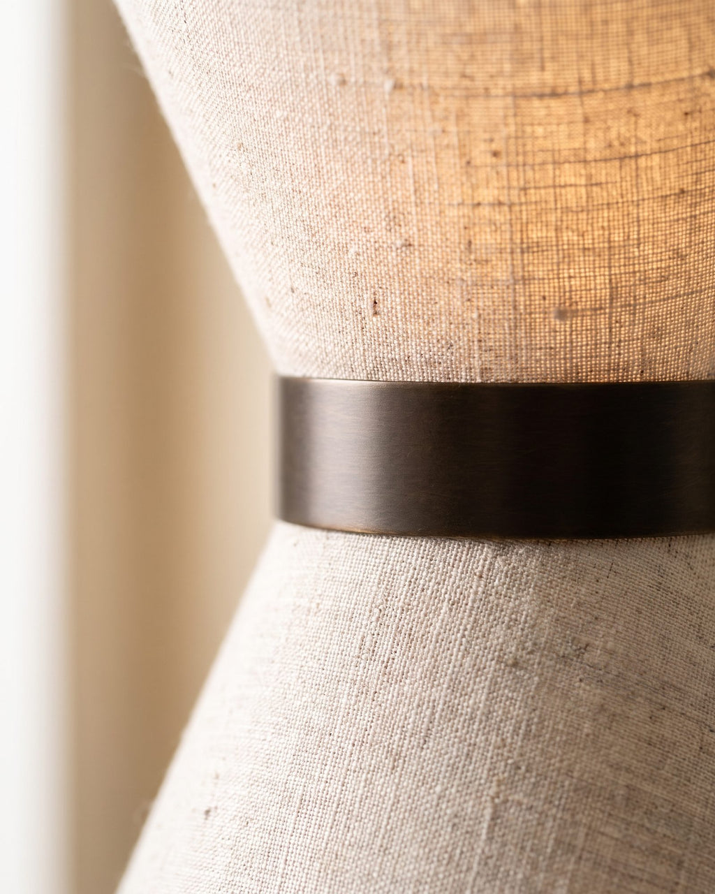Macro of the oatmeal linen weave and aged bronze band, lit from within