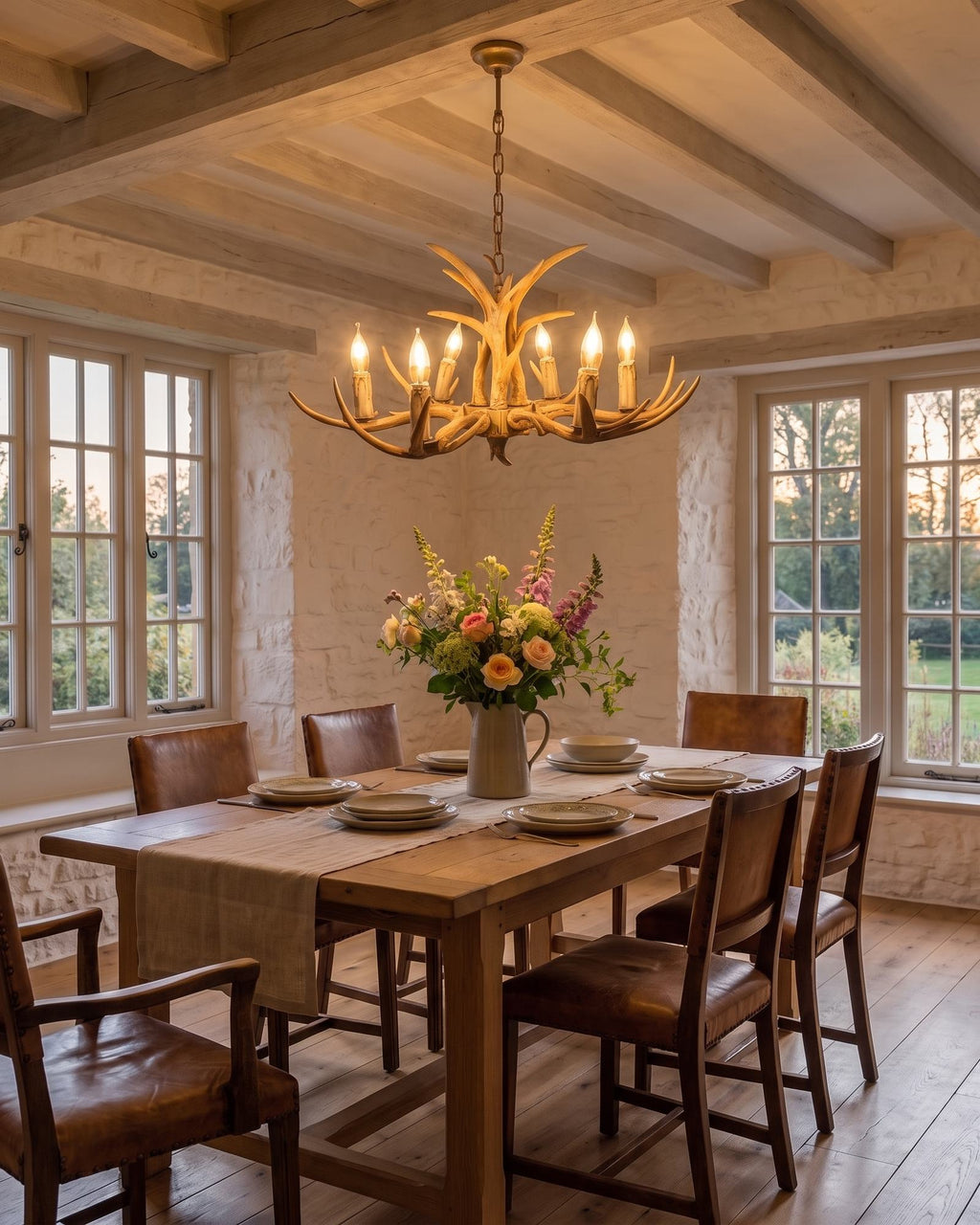 The six-light antler chandelier glowing over a laid table in a rustic dining room at dusk
