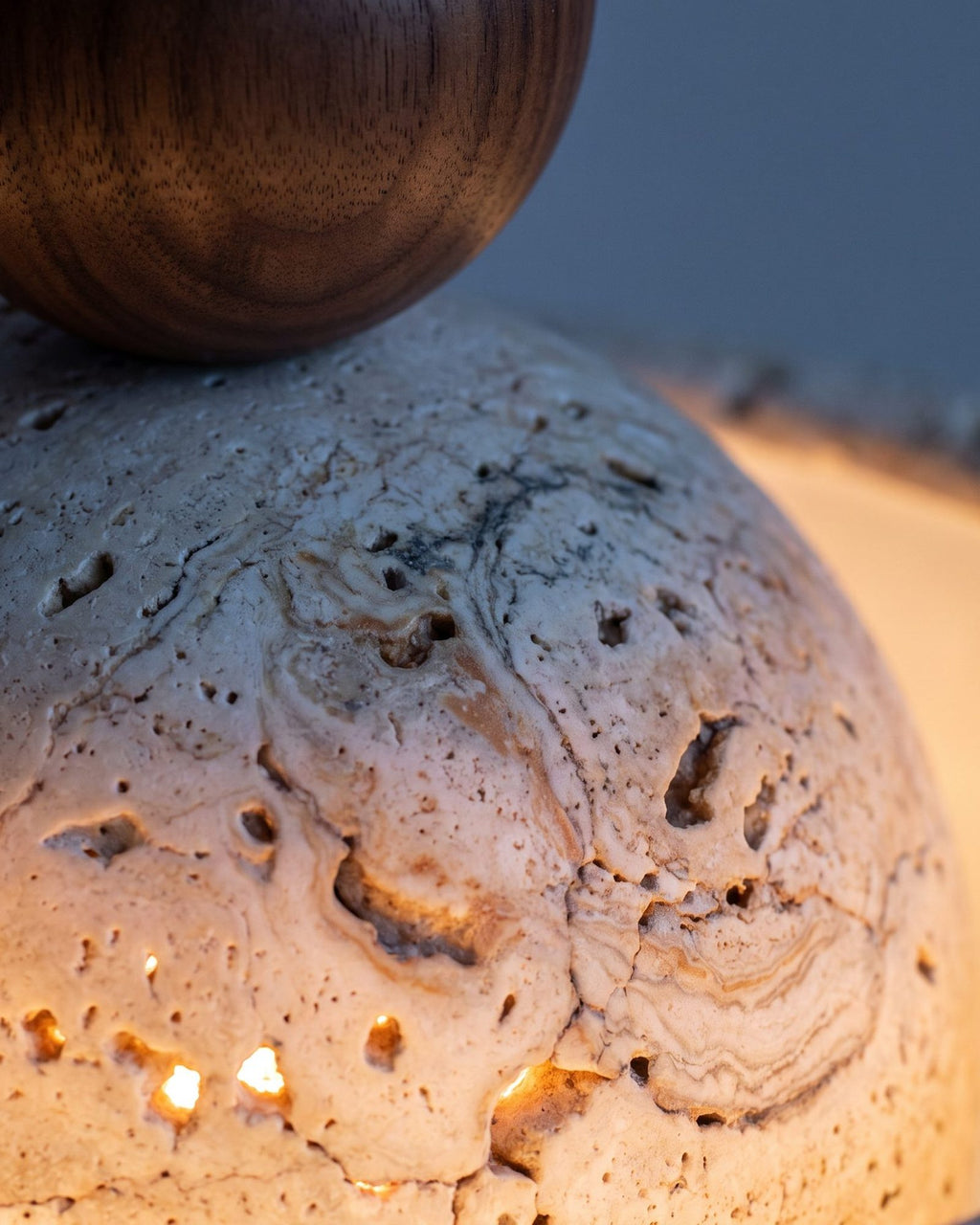 Macro of the travertine shade — natural pitted stone lit warmly from within