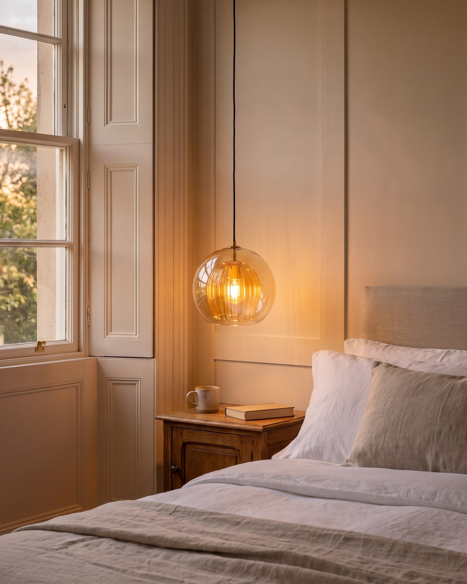 Zoey amber double-glass globe pendant glowing warm beside a bed at dusk