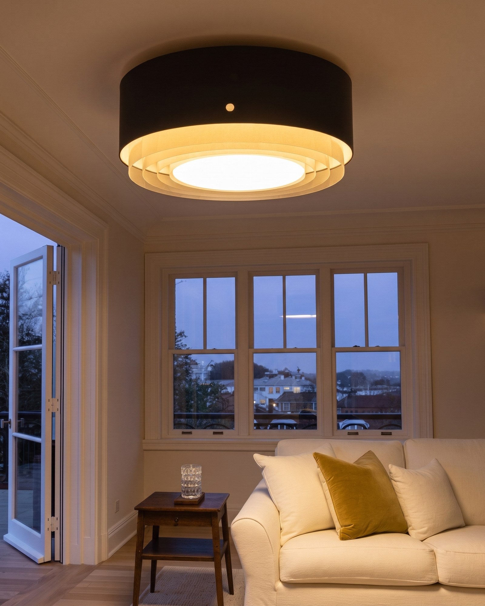 Black drum semi-flush ceiling light glowing warm in a living room at early evening