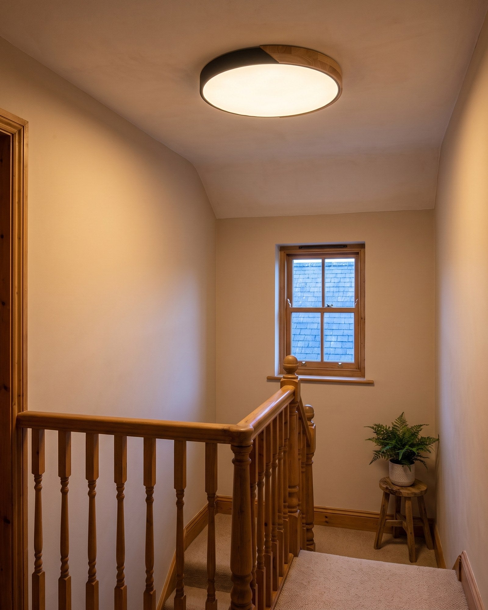 Black ultra-thin wood-trimmed ceiling light glowing warm on a landing at early evening
