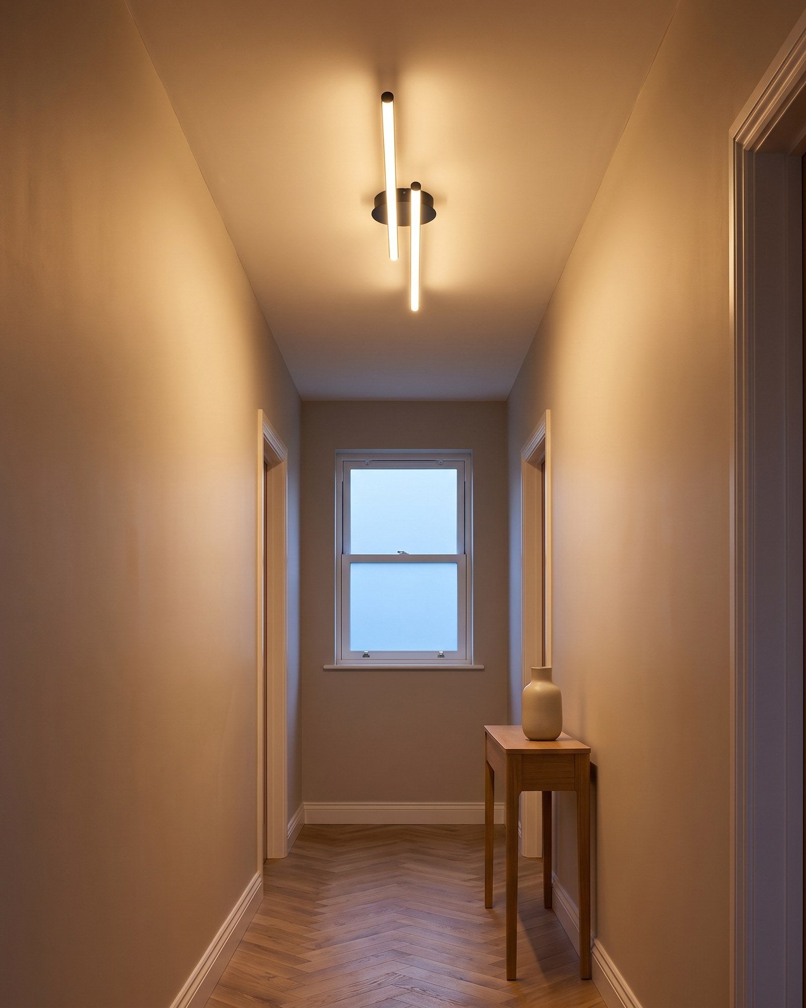 Twin-bar black LED flush ceiling light glowing warm in a hallway at early evening