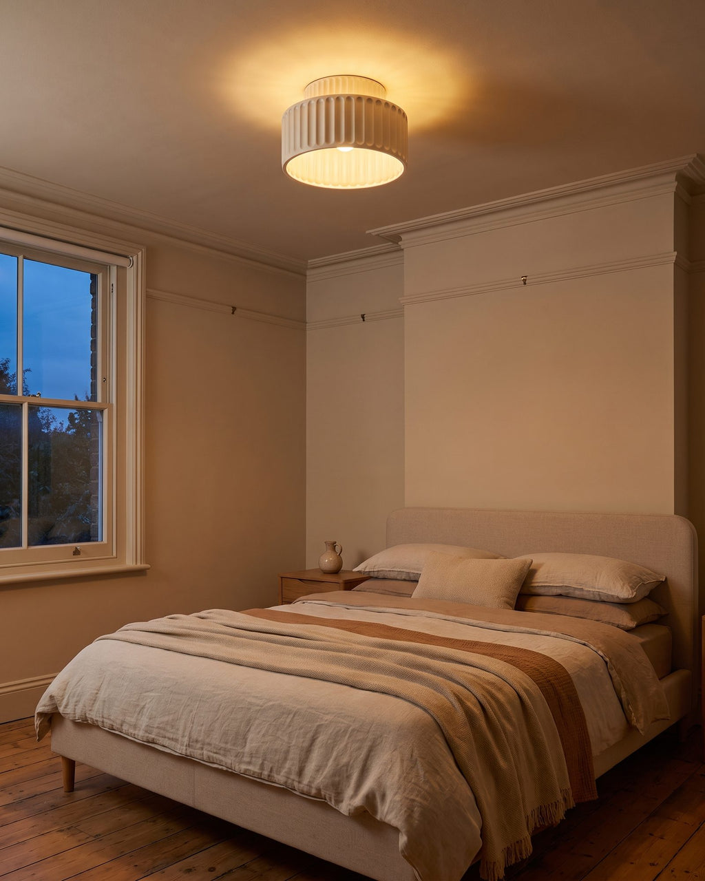 Cream pleated bowl ceiling light glowing warm in a bedroom at early evening