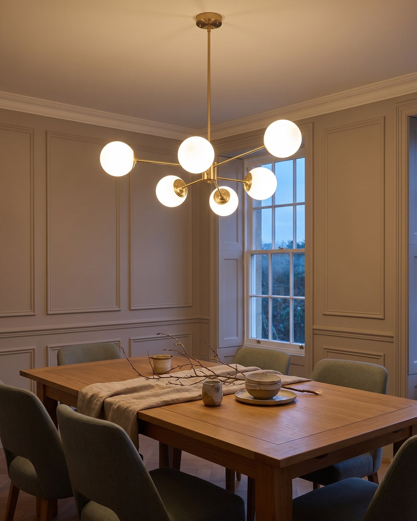 Brass six-light opal globe chandelier glowing warm over a dining table at early evening