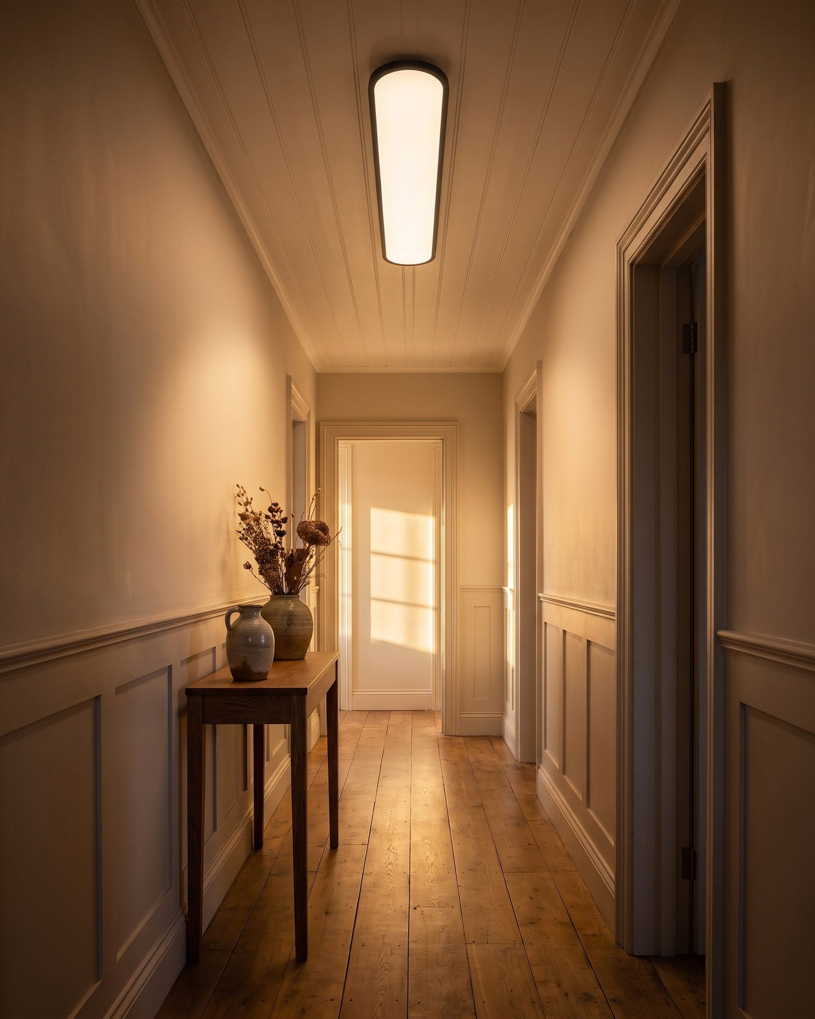 Black ultra-thin pill LED ceiling light glowing warm along a hallway at early evening