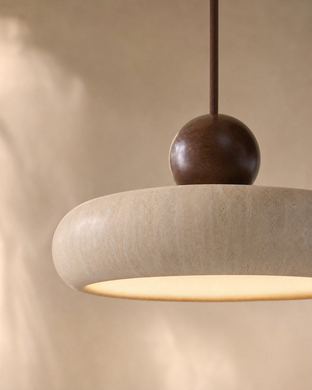 Close-up of the natural travertine stone round pendant with a turned wood sphere, warm glow beneath the smooth stone shade