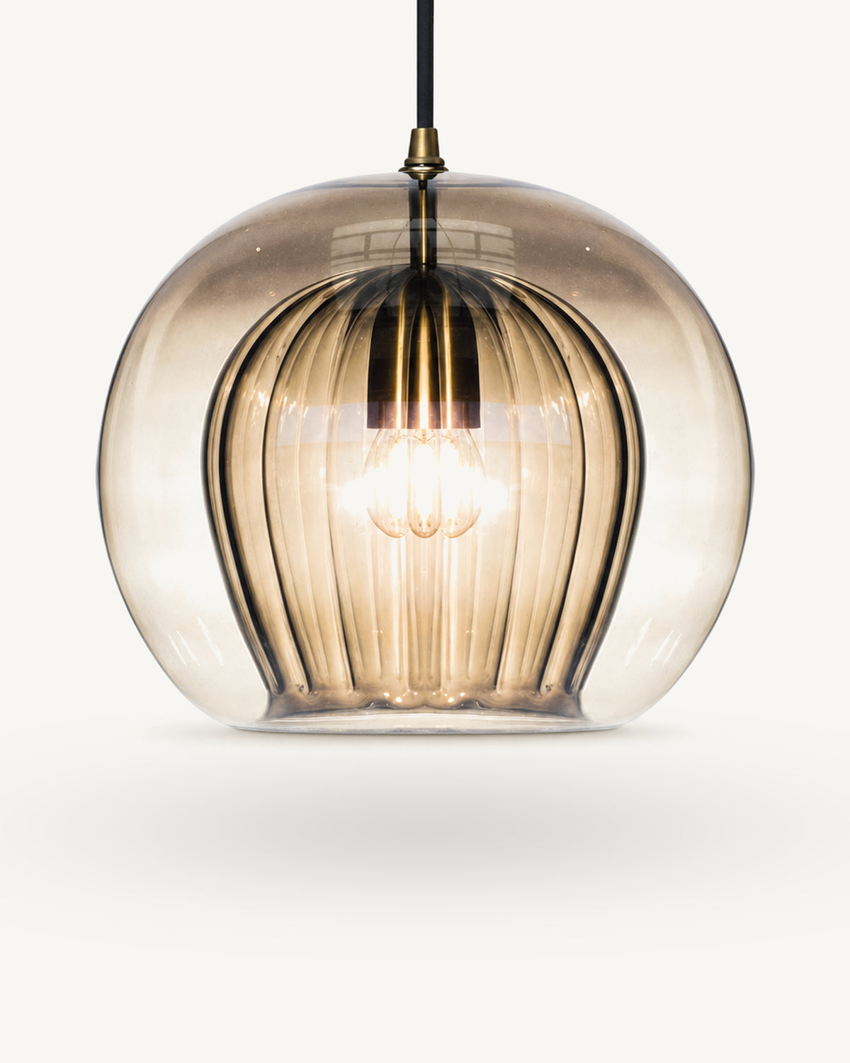 Zoey glass pendant light in Amber, warm cognac-toned glass shading lighter towards the base, over a ribbed inner shade, brass-finish lampholder on a black flex.
