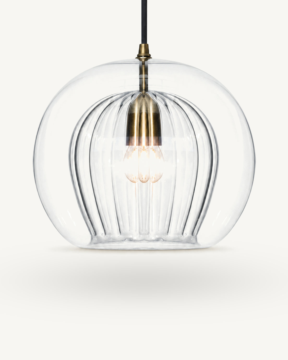 Zoey glass pendant light in Clear, a smooth outer glass globe over a ribbed inner shade, brass-finish lampholder on a black flex, shown against a plain light background.