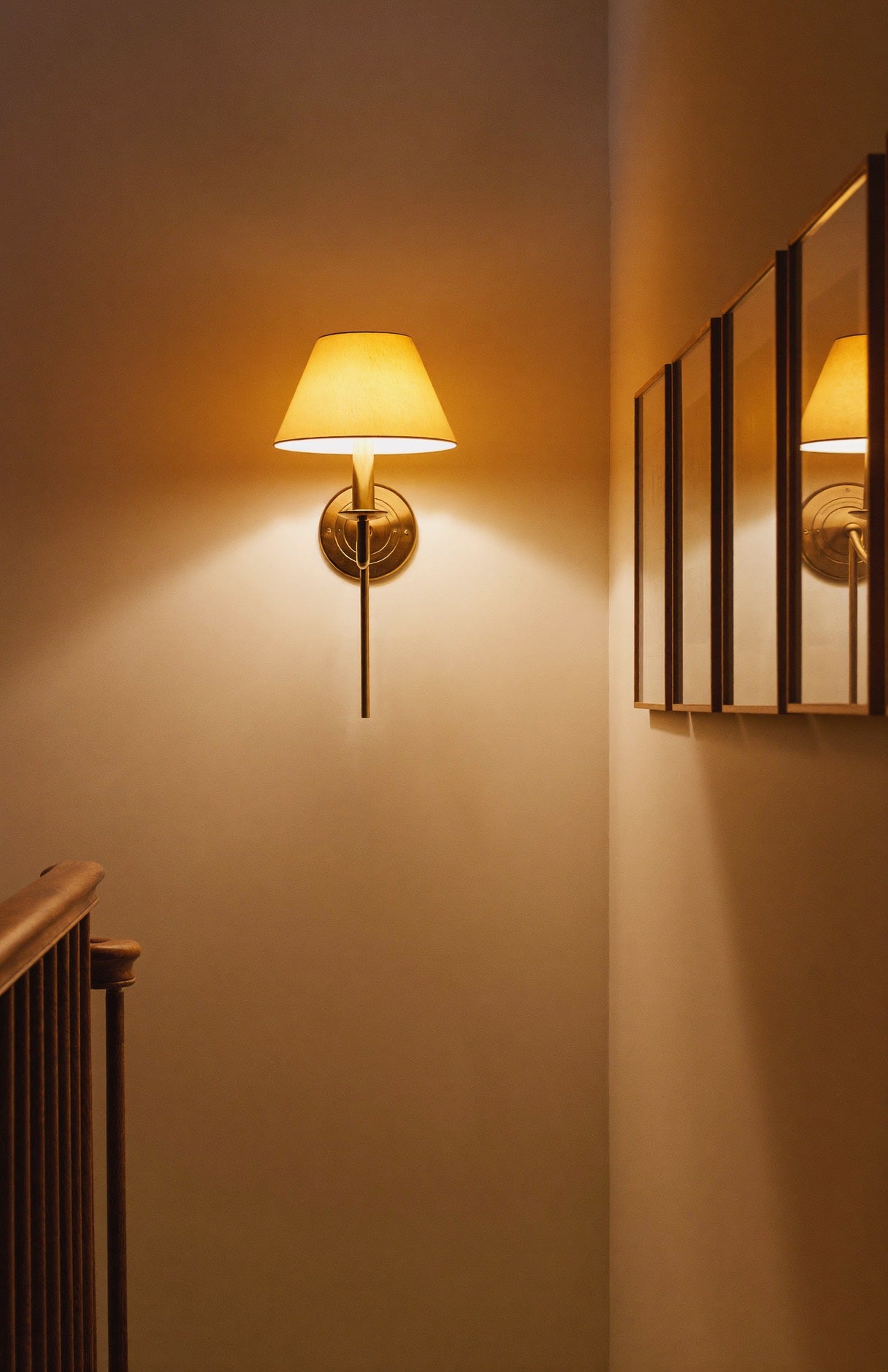 A brass wall light glowing softly on a stairway landing in the evening